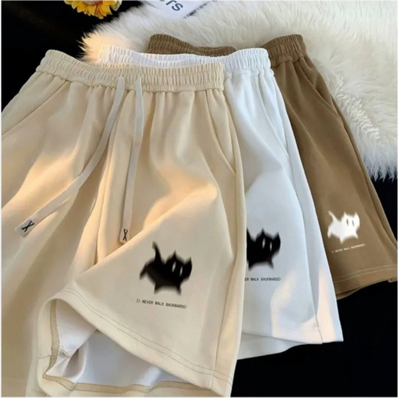 Three pairs of shorts in beige, white, and brown with black cat designs on a soft surface.